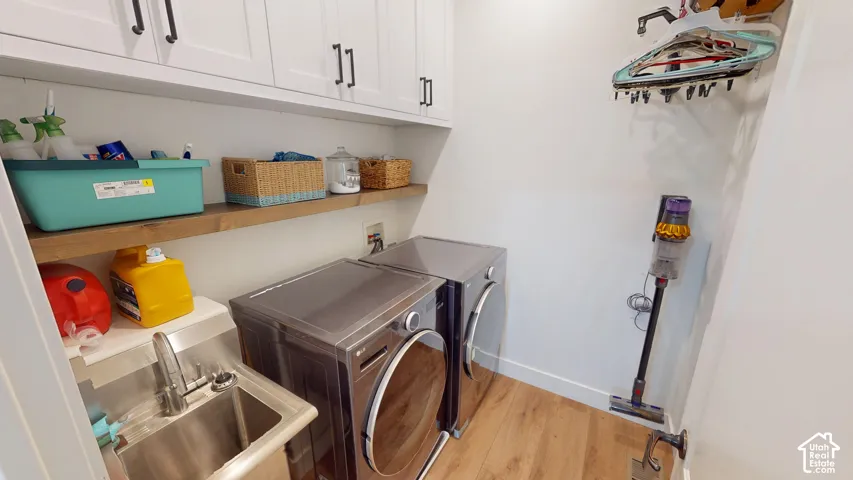Utility room featuring wood-finish flooring, white shaker-style cabinetry, open wood shelving, and a stainless steel utility sink with a high-arch faucet