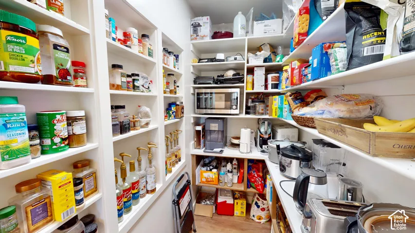 Walk-in pantry featuring white floor-to-ceiling built-in cabinetry, multiple tiers of fixed shelving, and wood-finish flooring