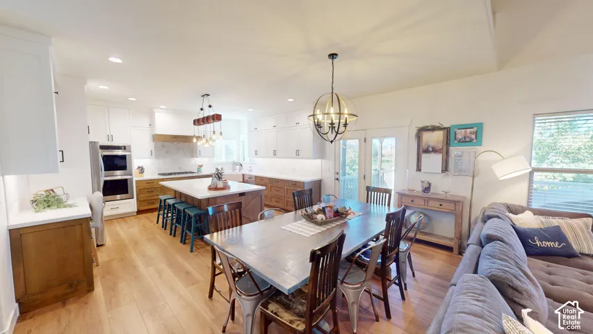 Kitchen and dining area featuring white cabinetry with contrasting wood-finish base cabinets, a center island with a stone-style countertop, built-in double wall ovens, recessed lighting, and wood-finish flooring