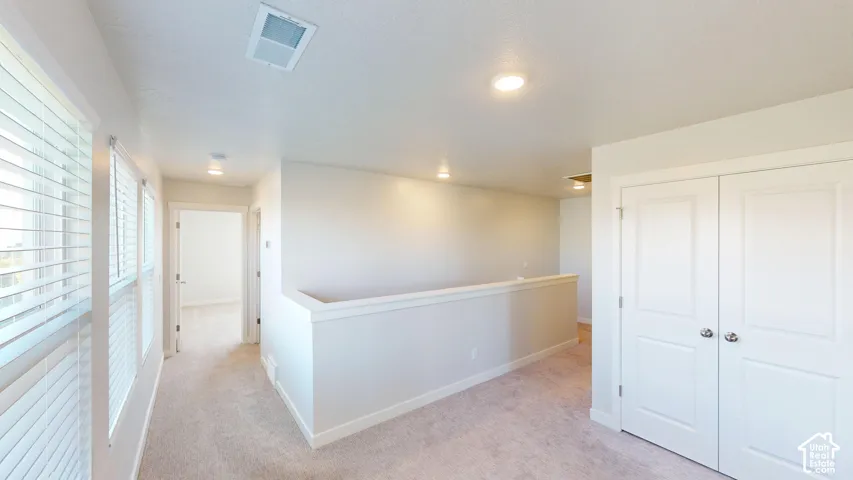 Open landing featuring neutral carpeting, recessed ceiling lighting, multi-panel double closet doors, and windows with horizontal blinds