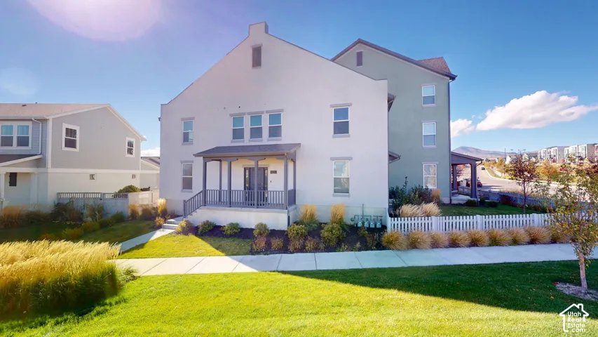 Multi-story residence featuring a stucco facade, covered front porch with a gable roof, and white picket fencing surrounding the perimeter