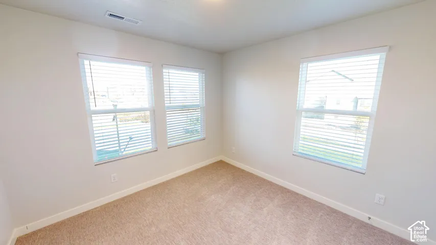 Neutral-toned walls, wall-to-wall carpeting, and three windows equipped with horizontal blinds