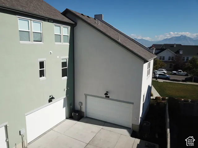 Multi-level exterior featuring stucco siding, two attached garages with white doors, concrete driveway, and mountain backdrop