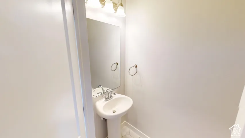 Pedestal sink with chrome faucet, wall-mounted mirror, three-light fixture, and circular towel ring