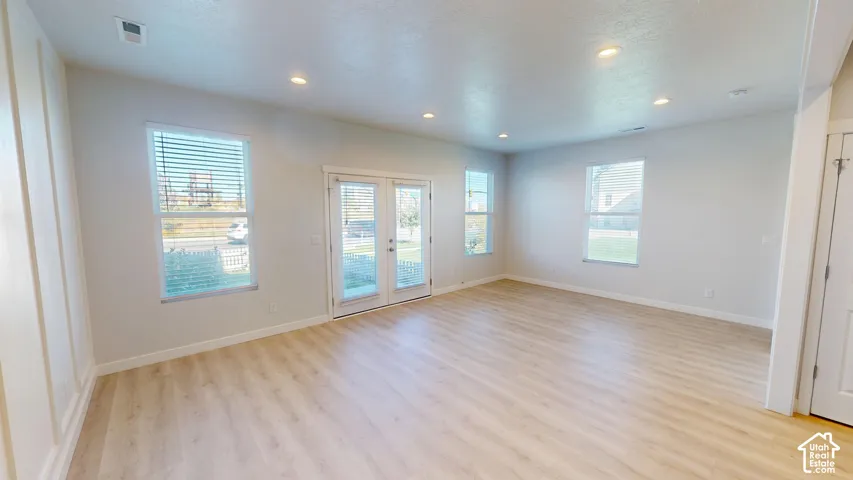 Open-concept room featuring light wood-finish flooring, recessed lighting, vertical wall molding, double-pane windows with horizontal blinds, and glass-paneled double doors