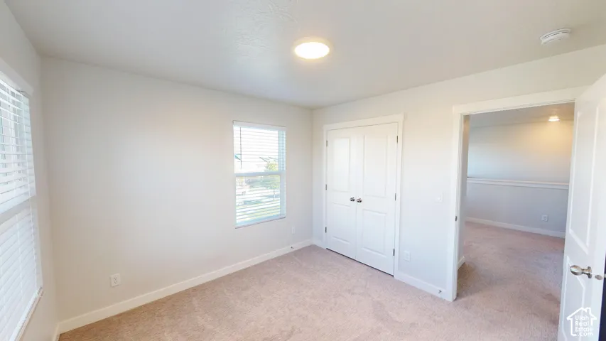 Neutral-toned room with plush carpeting, dual-panel closet doors with brushed nickel hardware, and multi-pane windows with horizontal blinds