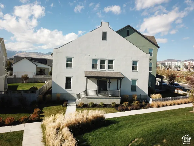 Multi-story exterior featuring light-colored stucco siding, a covered front porch, mountain backdrop, and professionally landscaped grounds with ornamental grasses