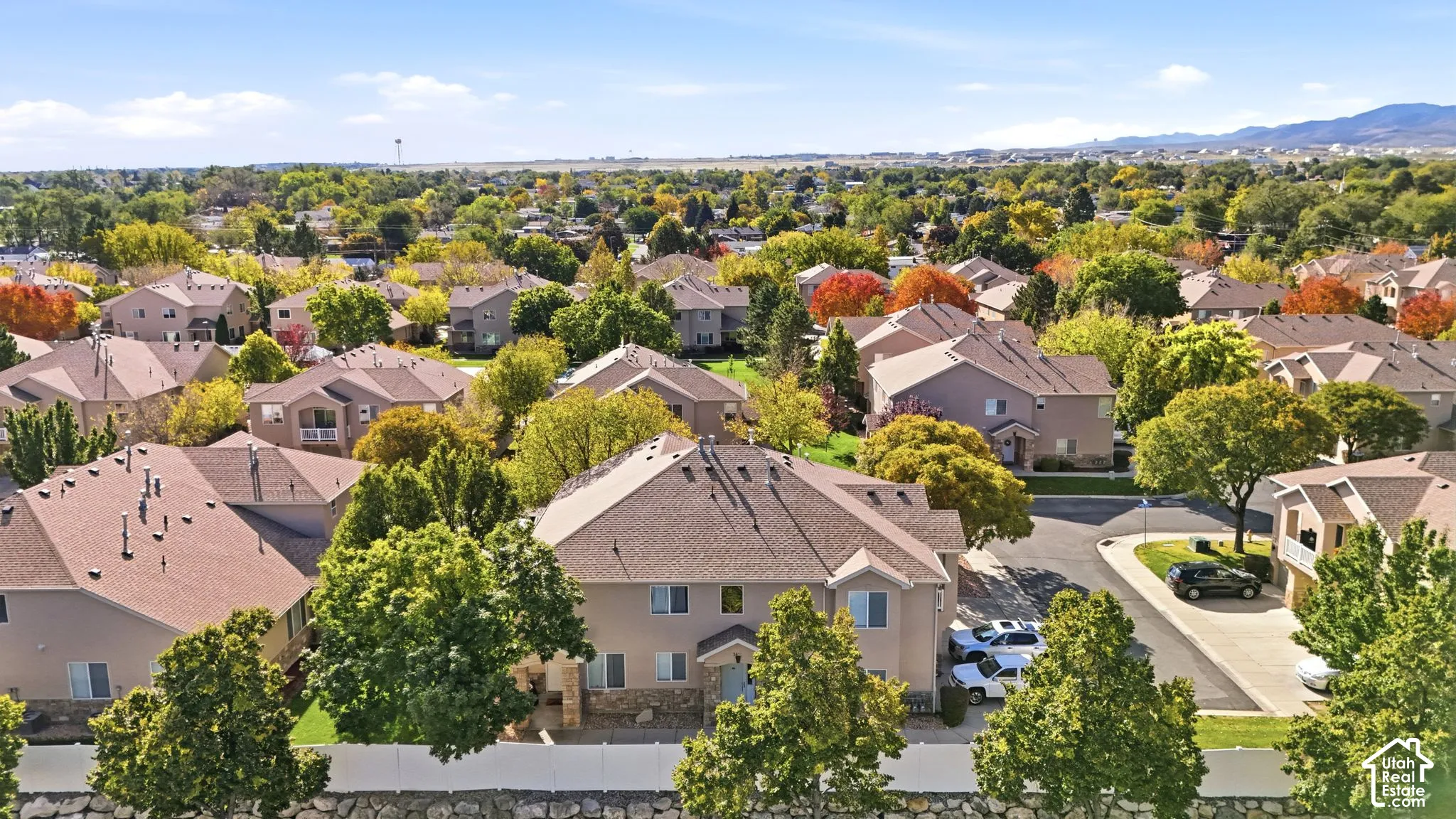 Aerial perspective featuring multi-story residential structures with pitched shingle roofing, integrated garage spaces, stone veneer accents, and surrounding established trees against a mountain backdrop