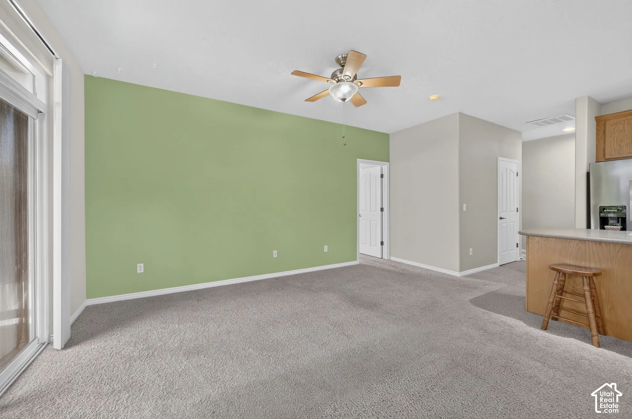 Living area featuring carpeted flooring, a ceiling fan with integrated lighting, sliding glass doors, and a kitchen island with wood-finish cabinetry