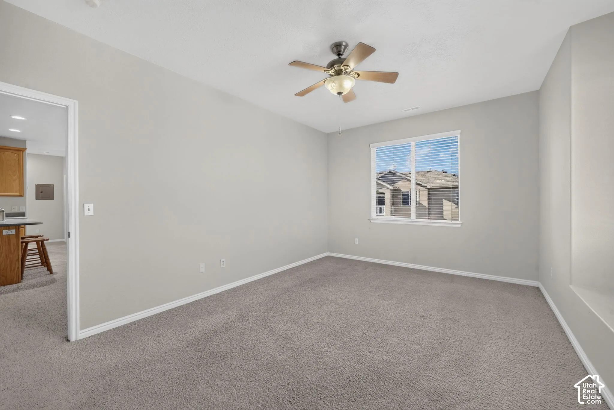 Neutral interior room featuring neutral carpeting, a ceiling-mounted light fixture with a fan, and a single-pane window