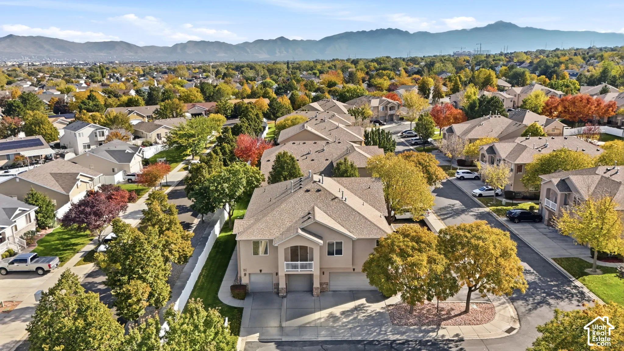 Multi-level residence featuring a stucco exterior, attached multi-car garage, second-story balcony with metal railing, asphalt shingle roof, and a mountain range backdrop