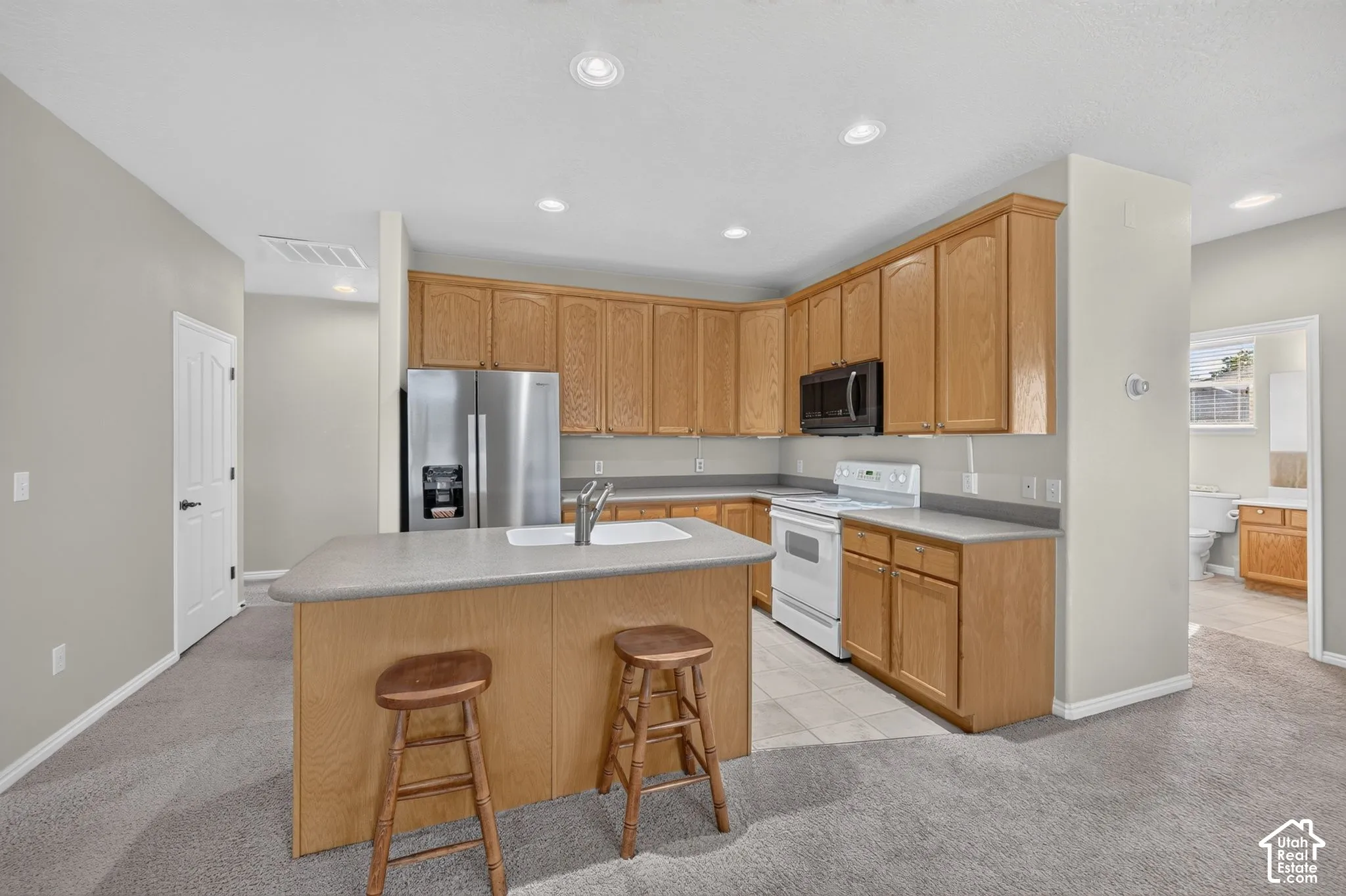 Kitchen featuring wood cabinetry, a central island with a drop-in sink, solid-surface countertops, and recessed lighting