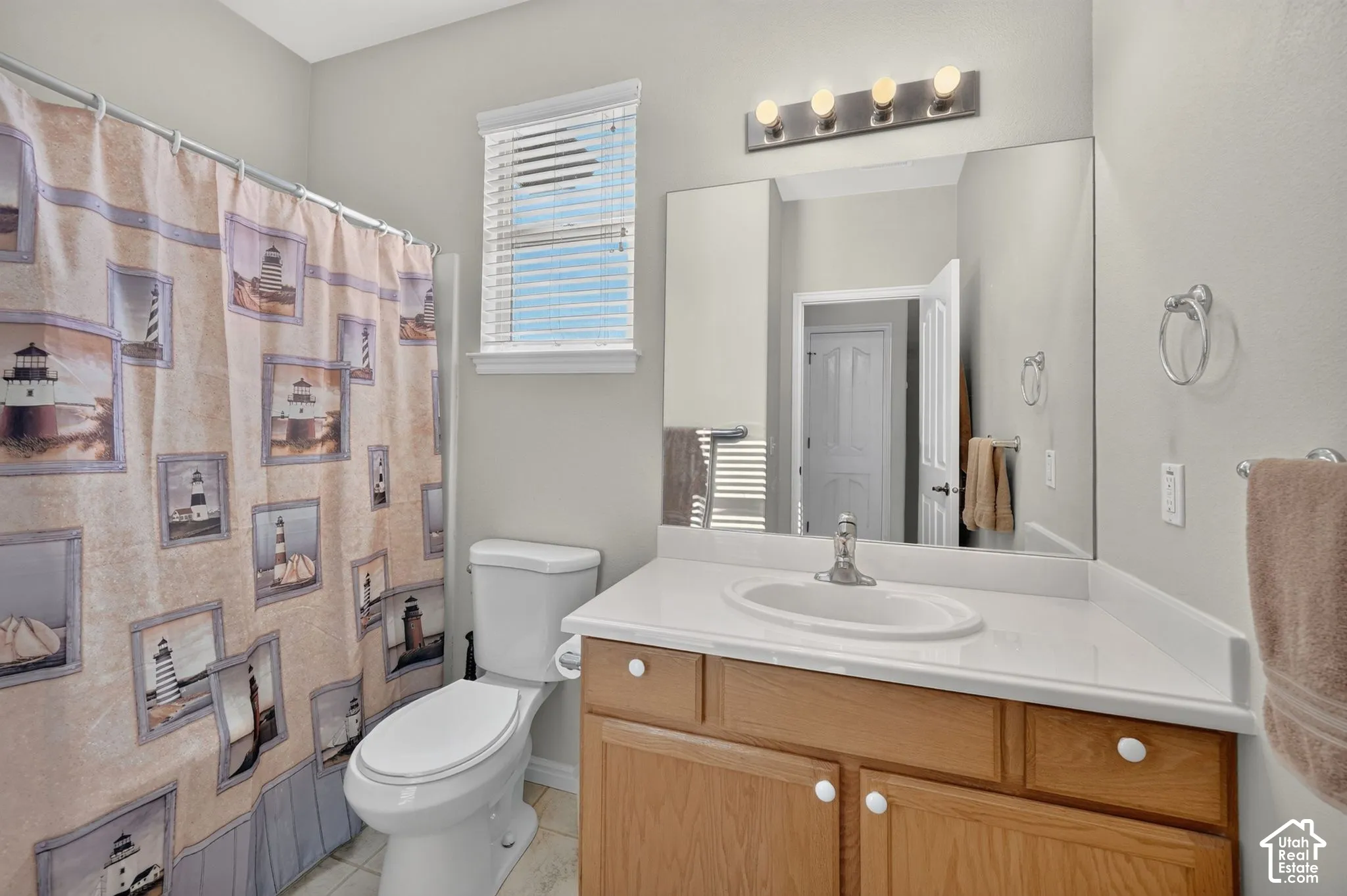 Bathroom featuring a wood-finish vanity with a composite countertop, integrated oval basin, polished chrome faucet, full-width wall-mounted mirror, and four-bulb overhead vanity lighting