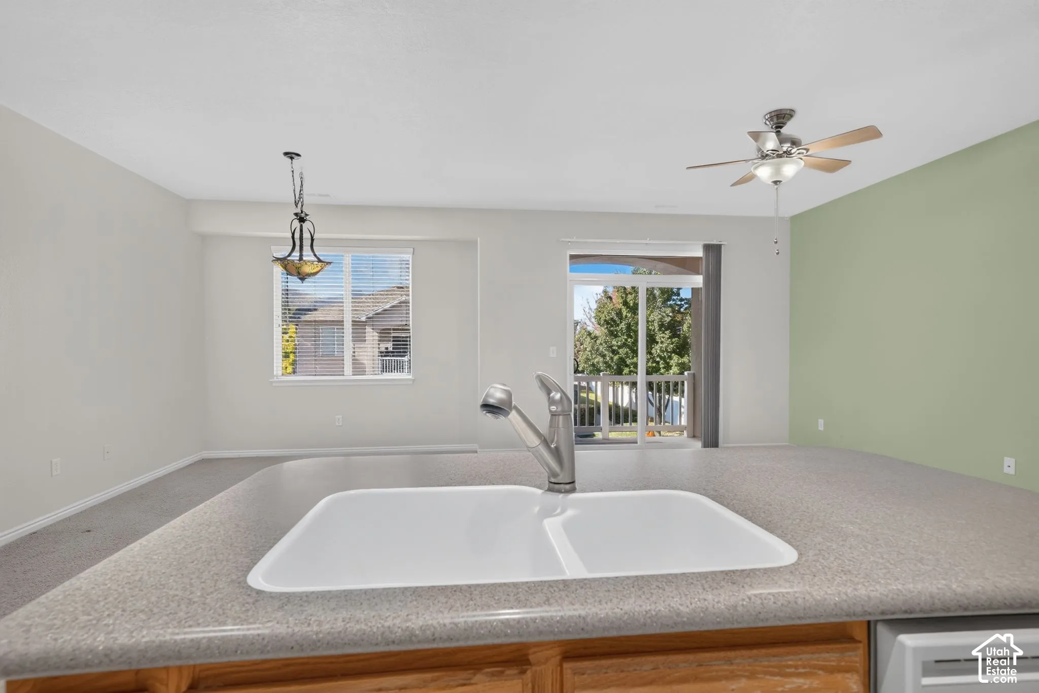Kitchen island featuring a dual-basin sink with a pull-down faucet, composite countertop, ceiling fan with integrated lighting, and decorative pendant lighting