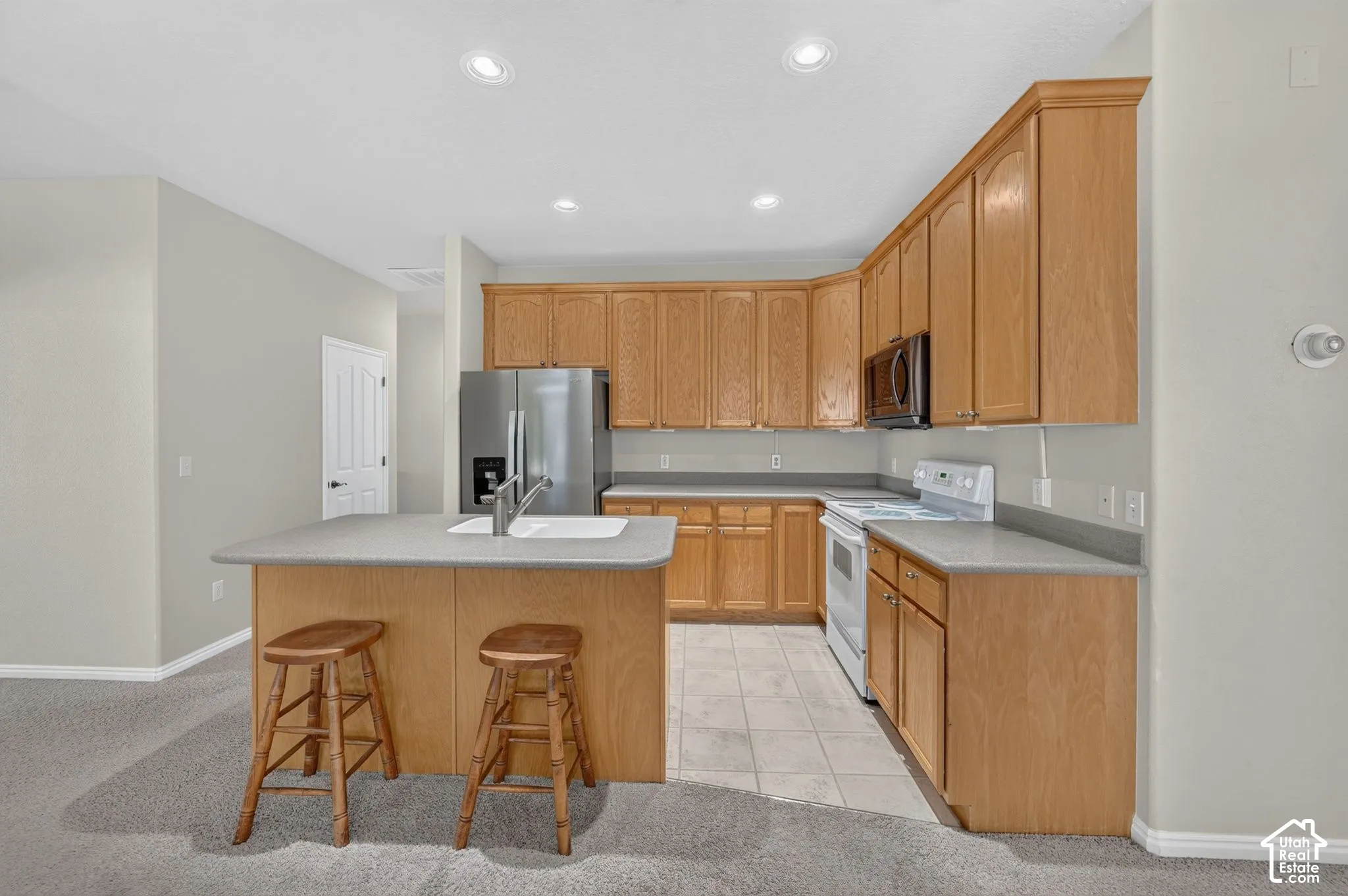 Kitchen featuring natural wood cabinetry, solid surface countertops, recessed lighting, and a central island with an integrated dual-basin sink