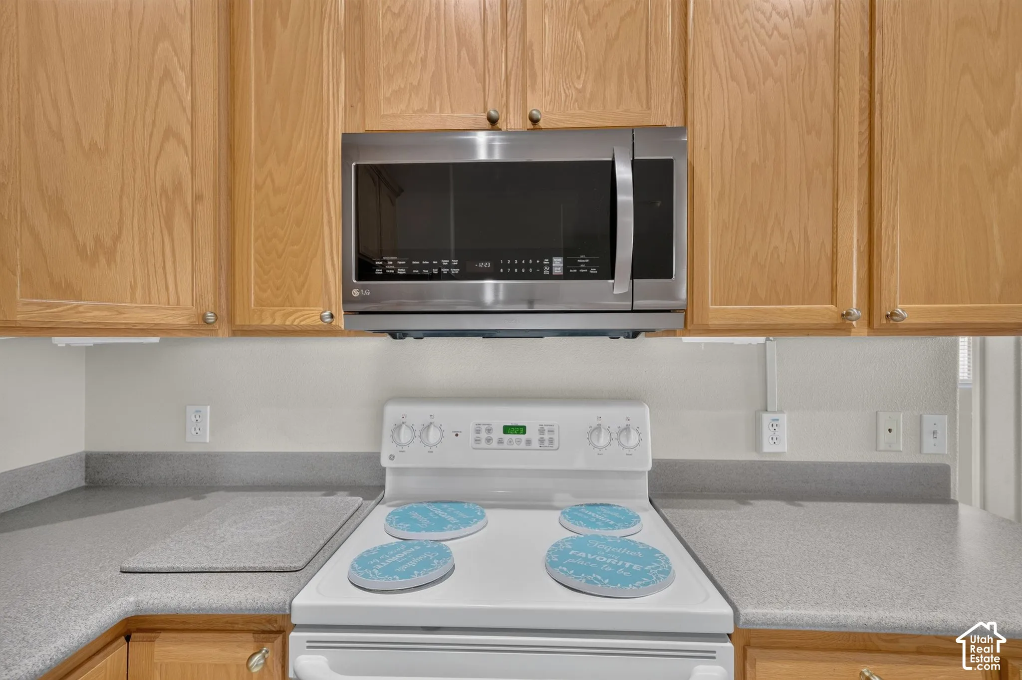 Natural wood cabinetry, stainless steel over-the-range microwave, white electric range, and solid-surface countertops