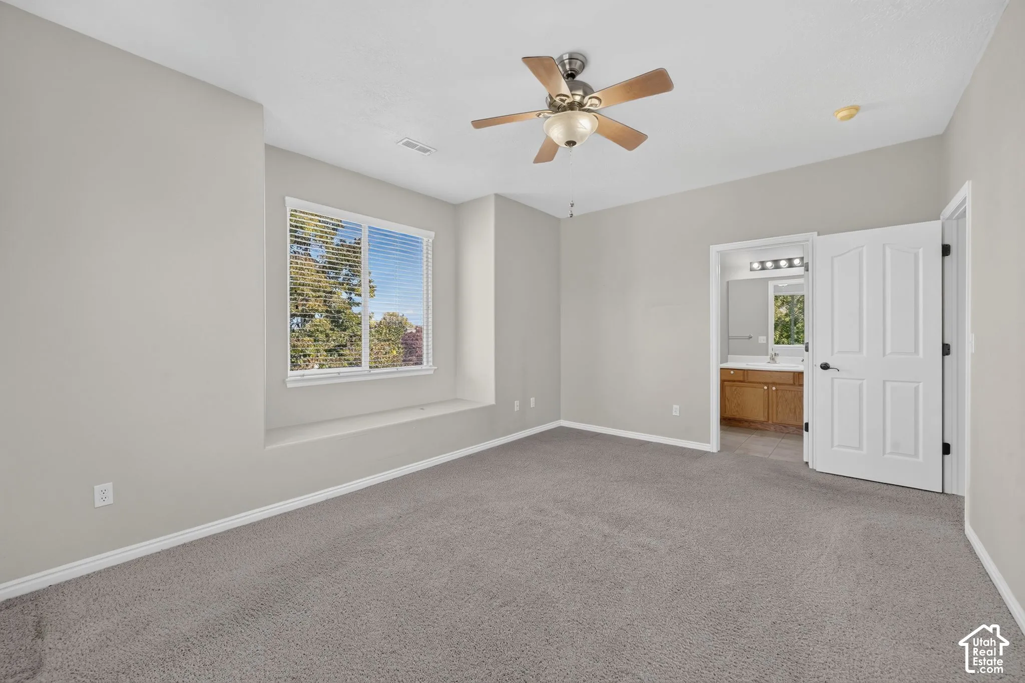 Neutral wall palette with plush carpeting, built-in window seat, ceiling fan with integrated light fixture, and arched-panel interior door