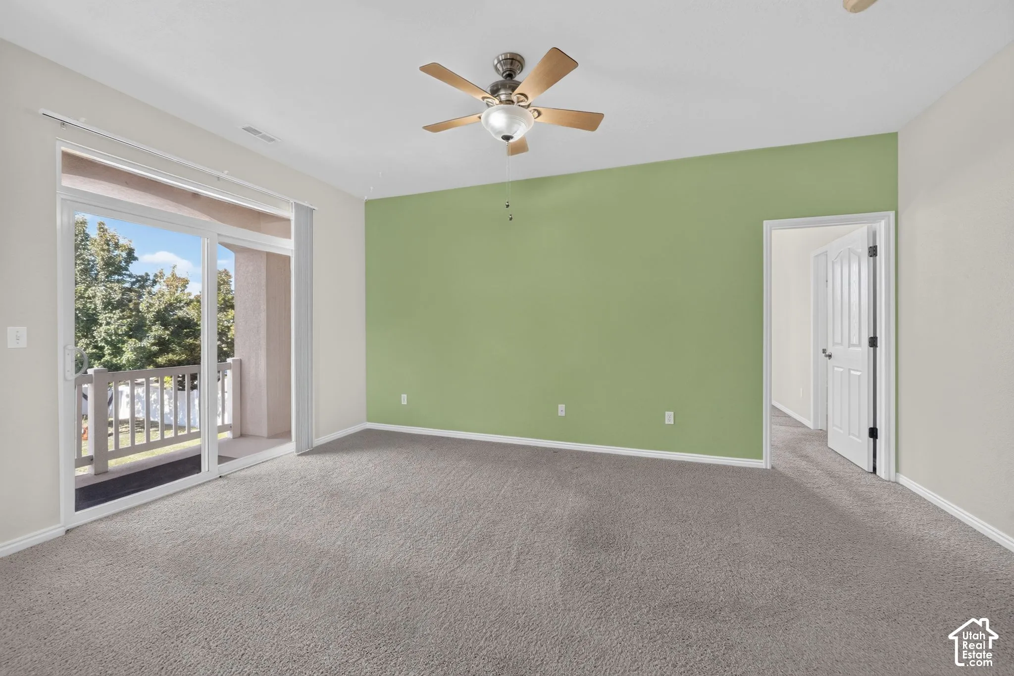 Spacious room featuring neutral carpeting, a central ceiling fan with integrated lighting, and a large sliding glass door
