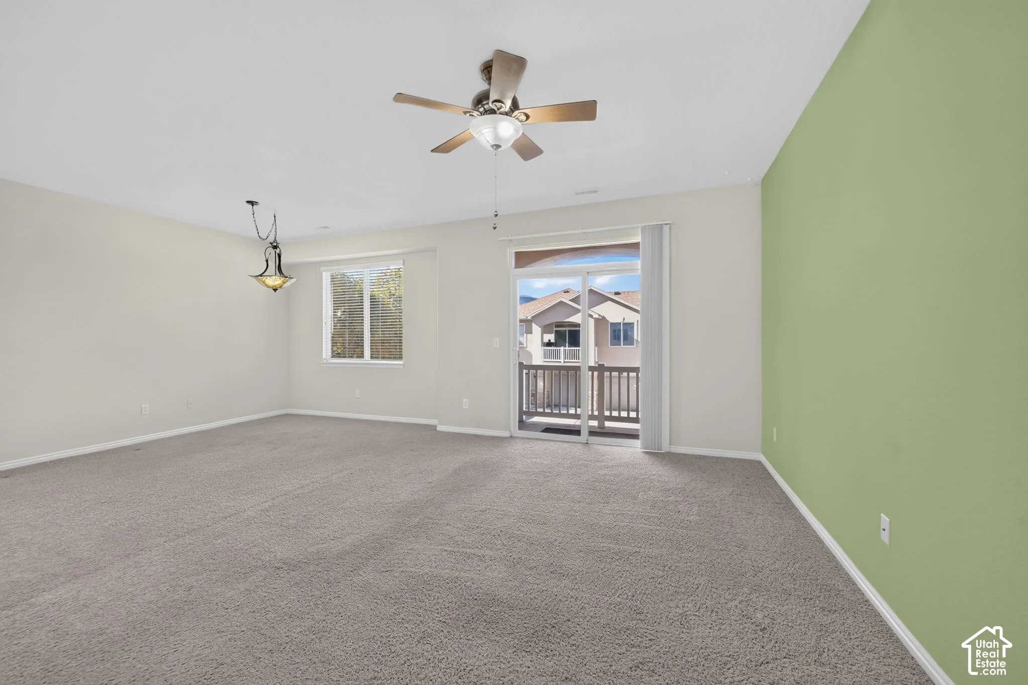 Neutral-toned interior featuring wall-to-wall carpeting, a ceiling fan with integrated lighting, a decorative pendant light, and a sliding glass door providing external access