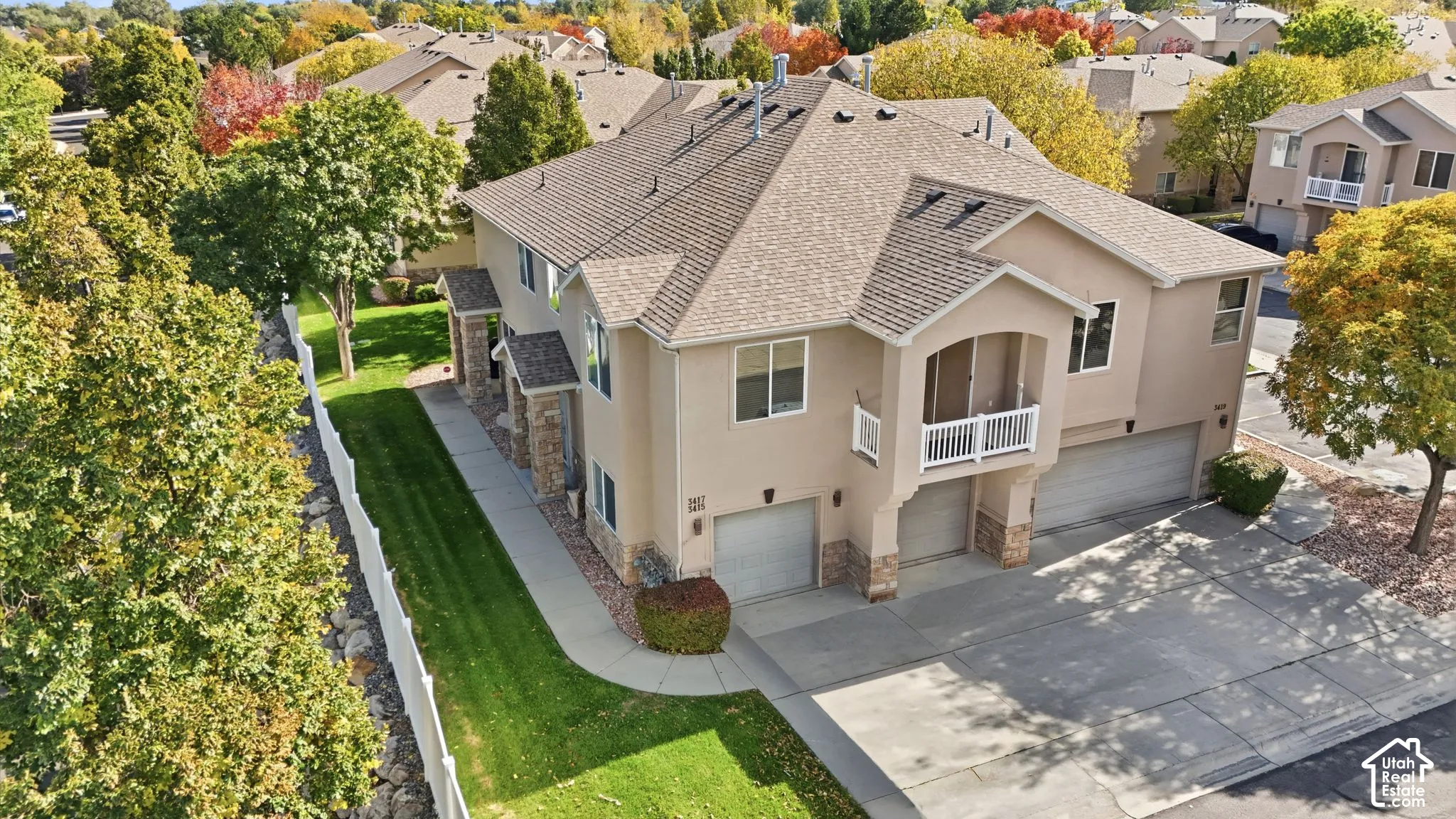 Multi-level exterior featuring tan stucco siding, stone veneer accents, multi-car garage, upper-level balcony with white railing, and concrete driveway