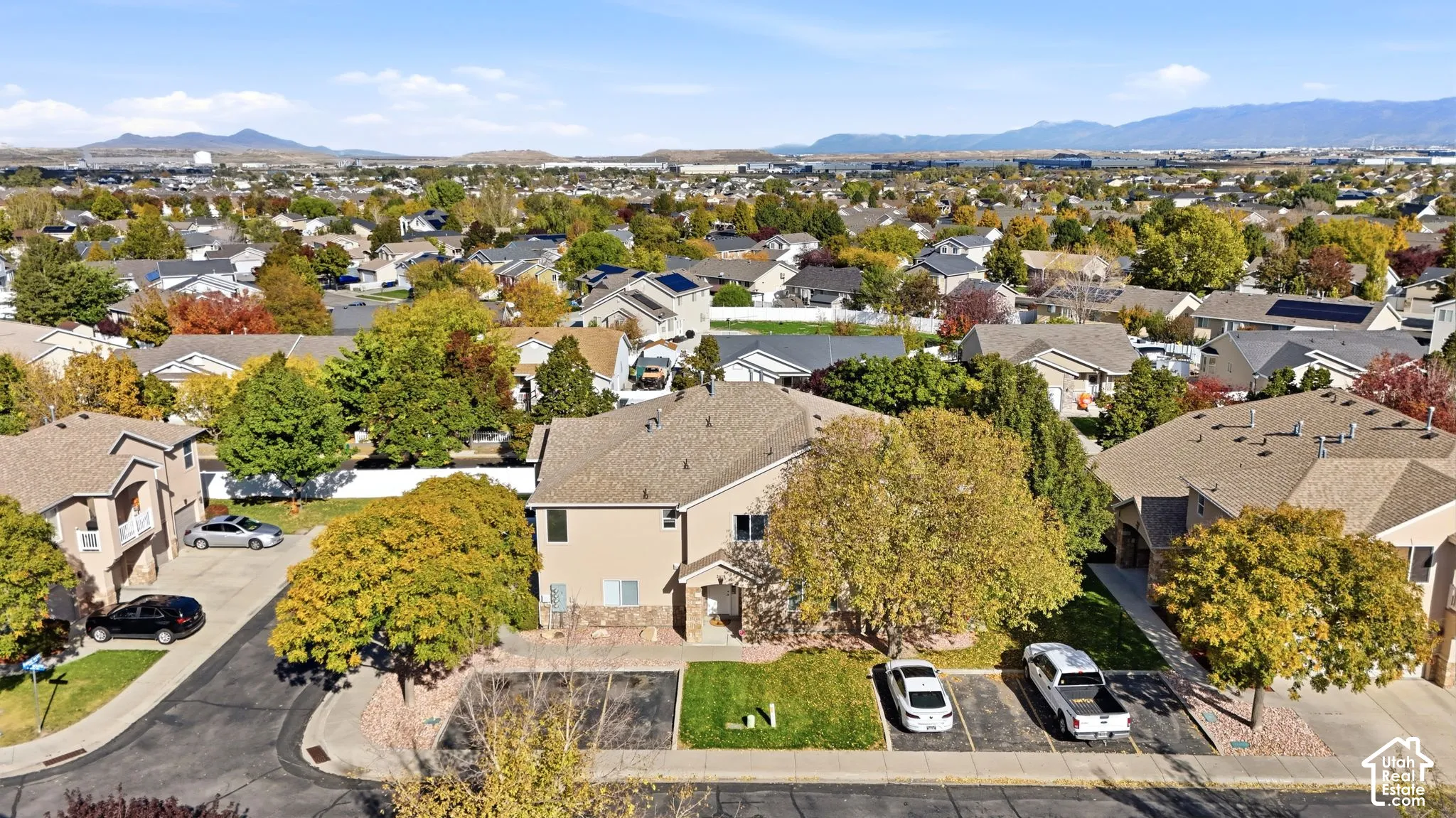 Aerial view featuring a two-story residence with tan stucco siding, stone veneer accents, an asphalt shingle roof, and dedicated surface parking