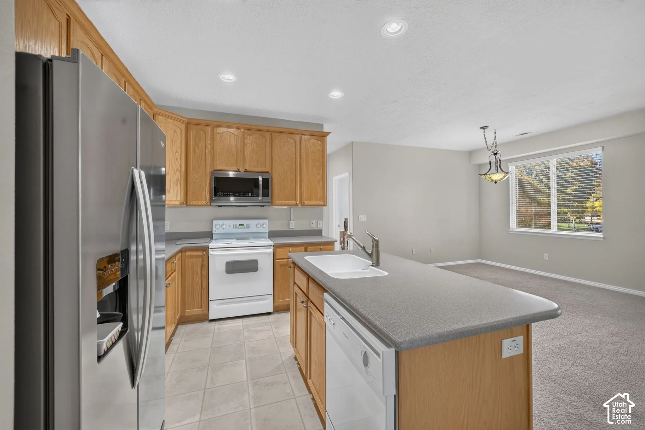Kitchen featuring wood cabinetry, stainless steel refrigerator, white appliance package, island with a dual-basin sink, and recessed lighting
