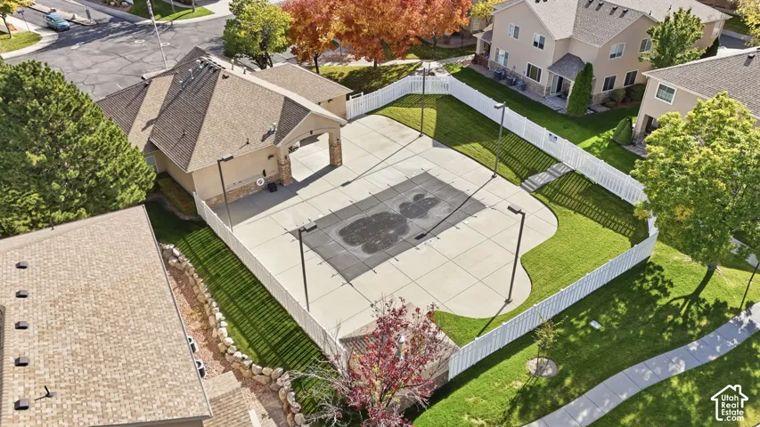 Fenced recreation area featuring a concrete sports court, high-mast lighting, stone-accented pavilion, and surrounding lawn