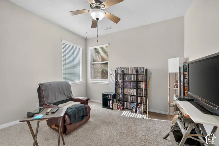 Room featuring neutral wall tones, plush wall-to-wall carpeting, two dual-pane windows with horizontal blinds, and a central ceiling fan with integrated lighting