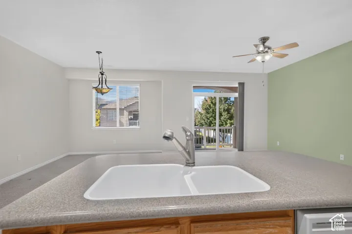 Kitchen island featuring a dual-basin sink with a pull-down faucet, composite countertop, ceiling fan with integrated lighting, and decorative pendant lighting