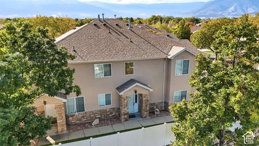 Two-story residence featuring a mixed stone and stucco exterior, hip roofline, mountain backdrop, and surrounding mature trees