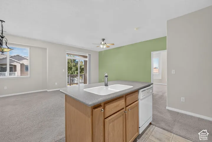 Kitchen island featuring wood cabinetry, a dual-basin sink, a faucet, and a dishwasher, accented by a sliding glass door