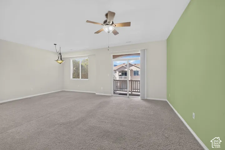 Neutral-toned interior featuring wall-to-wall carpeting, a ceiling fan with integrated lighting, a decorative pendant light, and a sliding glass door providing external access