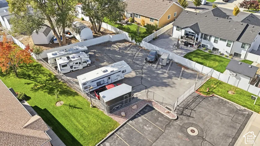 Paved parking area featuring designated spots, chain-link and vinyl privacy fencing, and mature trees