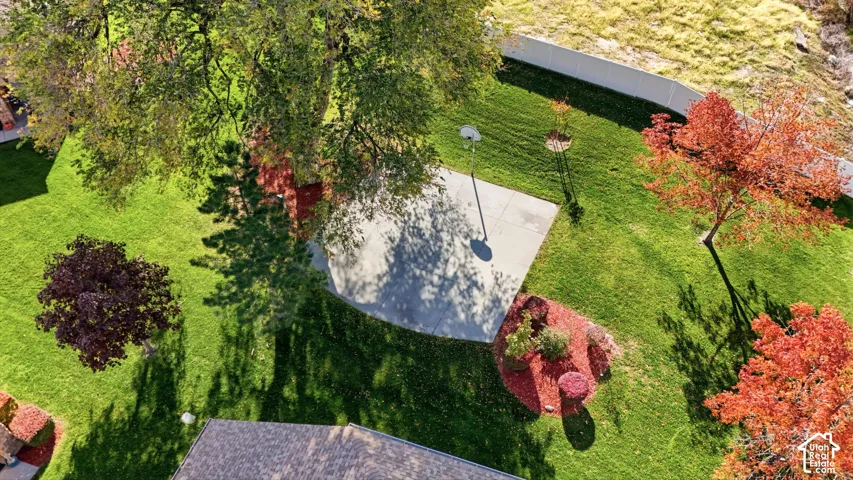 Expansive backyard featuring a concrete sport court, mature trees, landscaped planting beds, and white vinyl perimeter fencing