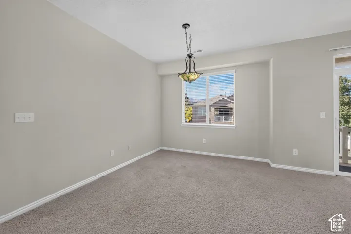 Neutral-toned interior space featuring wall-to-wall carpeting, an inset window, a decorative pendant light fixture, and a sliding glass door