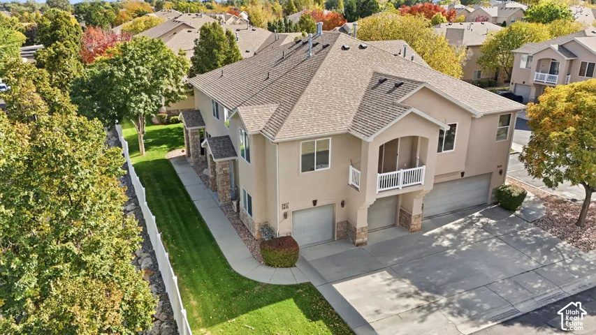Multi-level exterior featuring tan stucco siding, stone veneer accents, multi-car garage, upper-level balcony with white railing, and concrete driveway