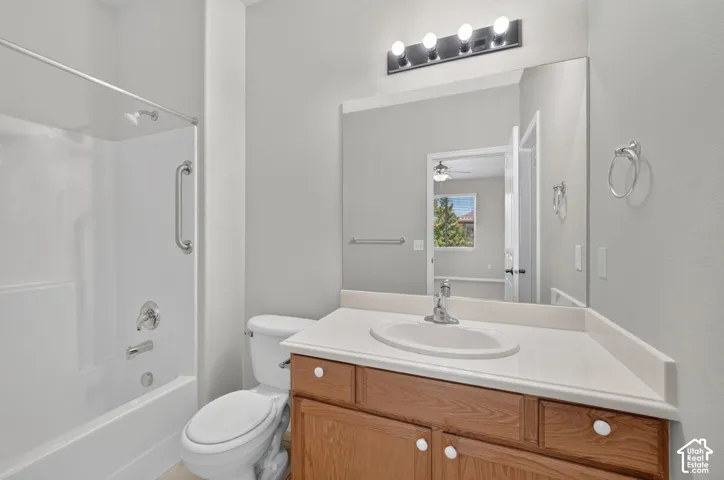 Bathroom featuring a vanity with a white solid-surface countertop and integrated sink, a large wall-mounted mirror, a four-light fixture, and a tub-shower combination with a metal grab bar