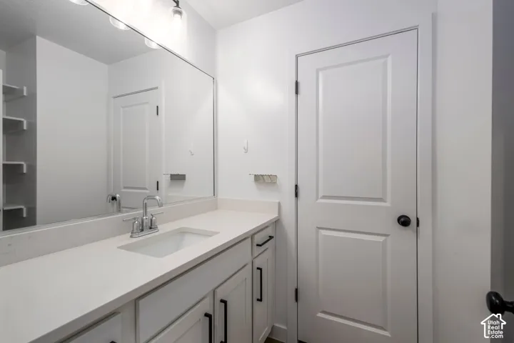 Hallway Full Bathroom featuring a light-toned vanity with a solid-surface countertop, an undermount sink, a full-width mirror, matte black hardware, and an interior door with a paneled design