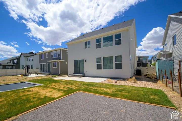 Two-story exterior featuring light-toned stucco siding, a concrete rear patio, multiple double-pane windows, and a fenced yard with gravel fire pit area.