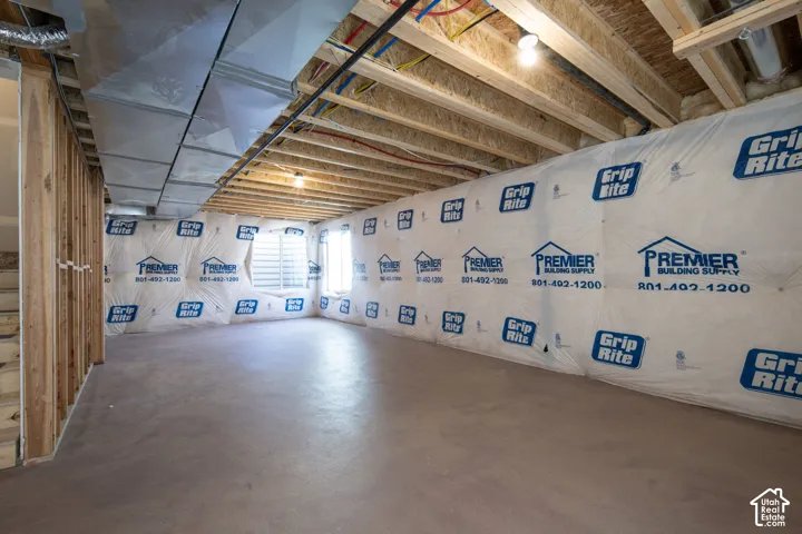 Unfinished space featuring exposed structural framing, concrete flooring, plastic vapor barrier wall covering, and metal ductwork