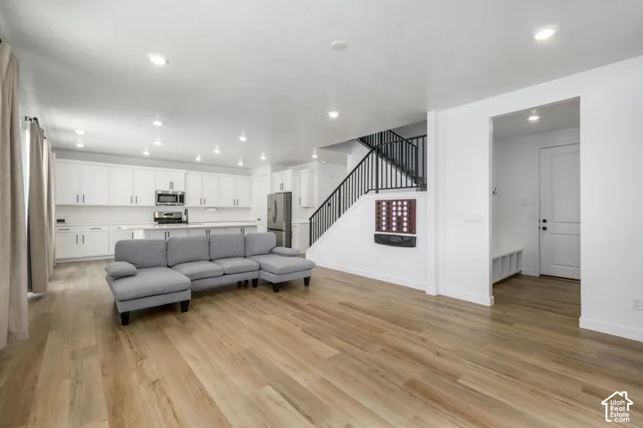 Open-concept interior featuring wood-finish flooring, recessed lighting, cabinetry with matte black hardware, a staircase with metal railings, and a built-in mudroom bench