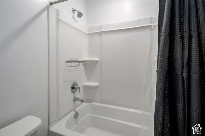 Hallway Full Bathroom. Bathtub and shower combination featuring a white molded surround, integrated soap shelving, polished chrome fixtures, and a shower curtain rod