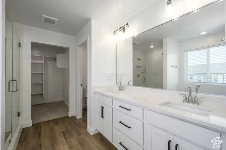 Master Bathroom. Dual-sink vanity with light-toned countertops and matte black hardware, glass-enclosed shower, expansive wall-to-wall mirror, and wood-finish flooring