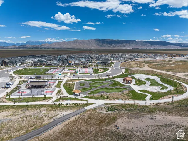 Community park featuring a paved pump track, multiple multi-use courts, covered pavilions, manicured lawns, and mountain backdrop