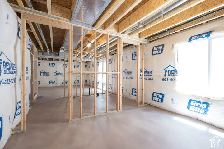 Unfinished interior space featuring exposed wood framing, concrete foundation flooring, open joist ceiling, and a large window