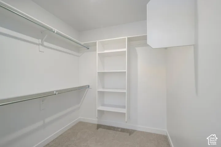 Master Bedroom Walk in closer #2. Walk-in closet featuring white built-in shelving, dual-tier metal hanging rods, and neutral carpeting