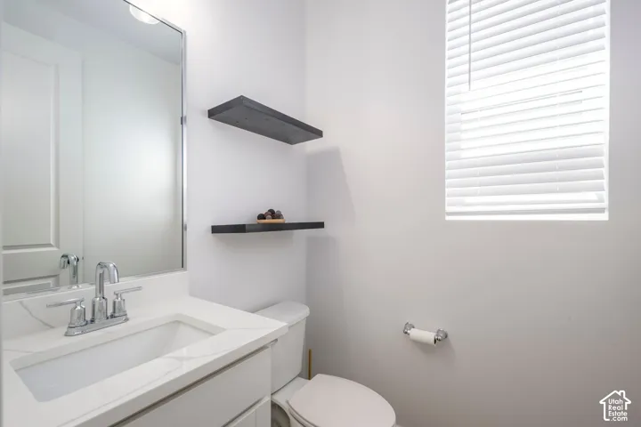 Bathroom featuring a vanity with a white countertop and rectangular undermount sink, chrome faucet, wall-mounted mirror, tiered black shelving, and window with white blinds