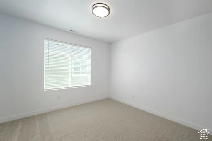 Bedroom #2. Neutral-toned interior space featuring light-colored wall-to-wall carpeting, a multi-pane window with integrated blinds, and a circular flush-mount ceiling light fixture