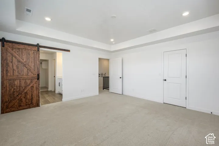 Master BR featuring a tray ceiling, recessed lighting, carpeted flooring, and a sliding wood-finish barn door
