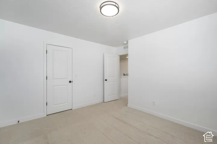 Bedroom #4 with large walk in closet. Interior space featuring neutral wall-to-wall carpeting, white walls, two-panel interior doors with matte black hardware, and a flush-mount circular ceiling light fixture